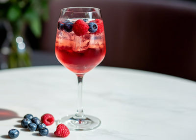 Close-up of Sleepy Berry Spritz in stemmed glass with ice and floating raspberries and blueberries on white tabletop