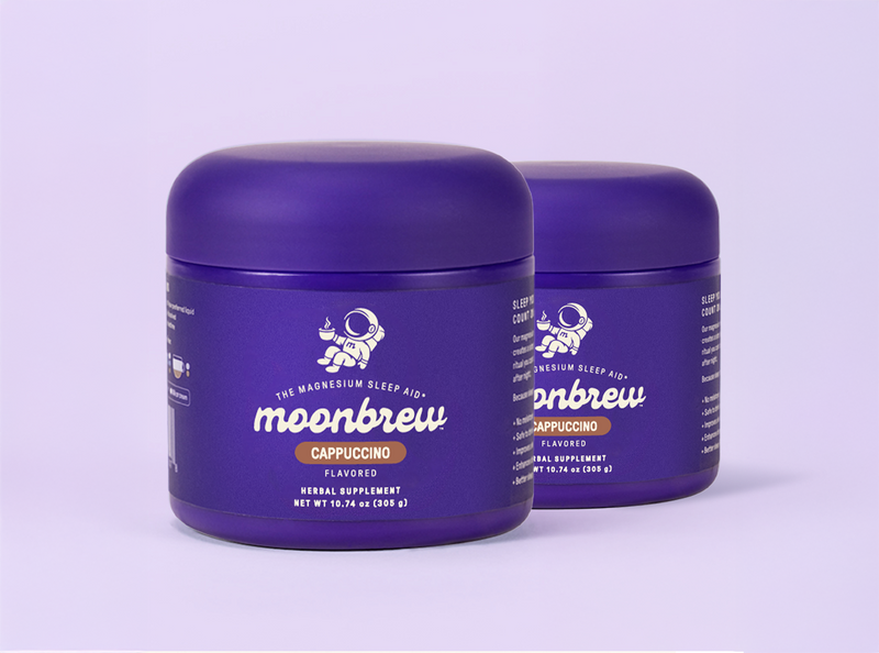 Front-left view of two MoonBrew Cappuccino magnesium sleep aid tubs showcasing purple packaging on a light lavender background