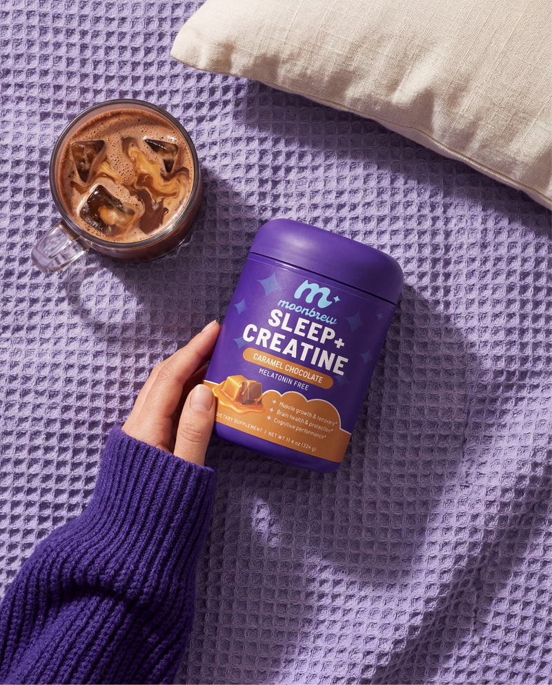 Top-down view of Sleep + Creatine jar (Caramel Chocolate) showing front label on a purple blanket next to an iced drink