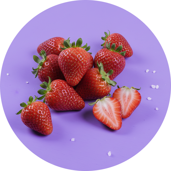 Ripe red strawberries with green tops, one halved to show interior, on purple surface with scattered white crystals.