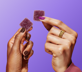Close-up of two MoonBrew sleep gummies held between fingers showing sugar-coated texture on purple background