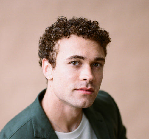 Man in a green jacket looking at camera against a beige background