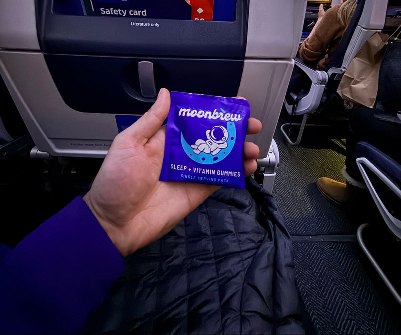 Front view of MoonBrew purple single serving packet of sleep vitamin gummies showcasing brand name and astronaut logo with airplane seatback background