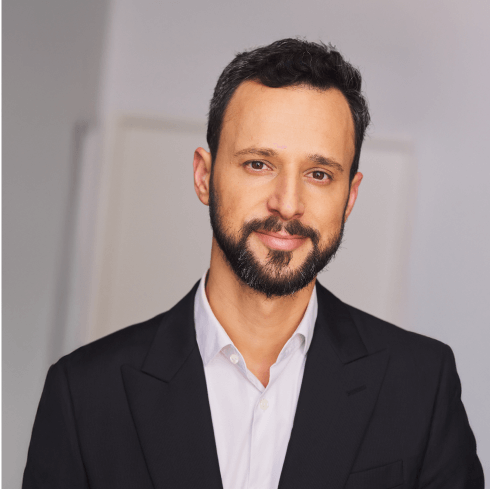 Smiling male physician (Dr. Joel Gator Warsh) portrait wearing a dark suit and white shirt against a neutral blurred background