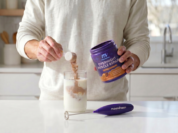 Person scooping Overnight Muscle Repair powder into a glass of milk on a bright kitchen counter with a MoonBrew frother beside it
