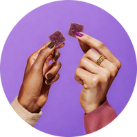 Close-up of two hands holding purple sleep vitamin gummies showcasing sugar-coated texture with solid purple background
