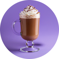 Footed clear glass mug of hot chocolate topped with whipped cream and chocolate drizzle