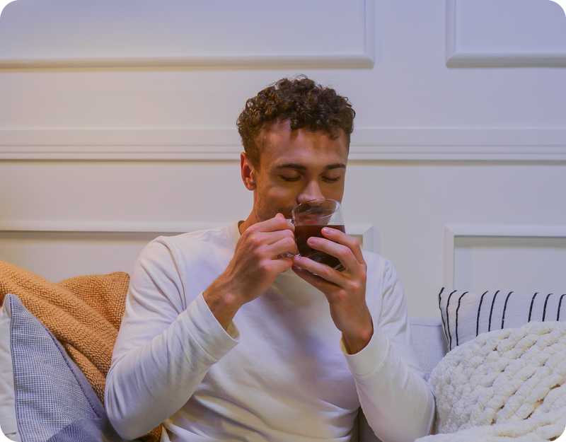 Man sipping a warm MoonBrew beverage on a sofa in a cozy living room