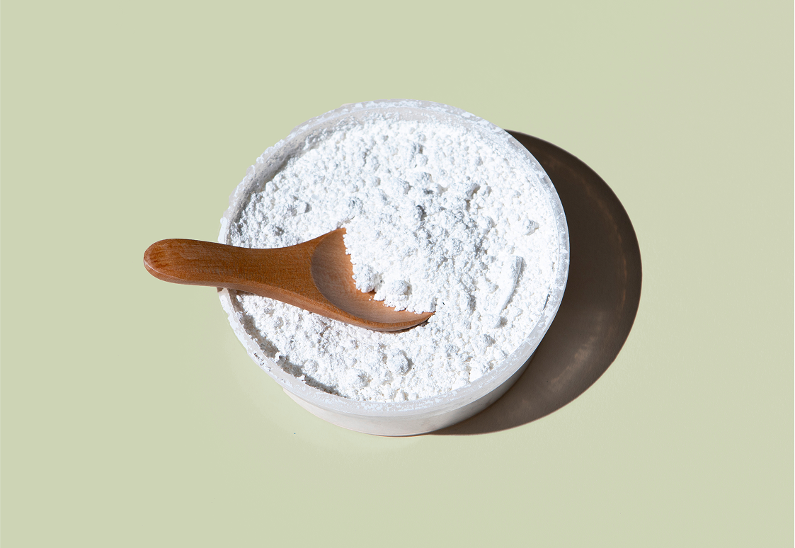 Overhead view of jar of white magnesium powder with wooden scoop showing fine texture on pale green background
