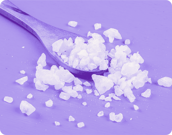 Close up of magnesium salt crystals on a wooden spoon showcasing coarse white granules on a purple tinted wood surface