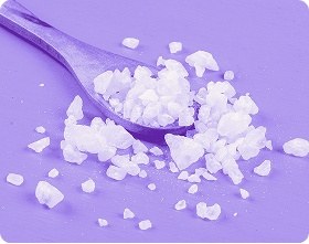 Close-up of a spoonful of white crystalline powder showcasing coarse granules on a purple background