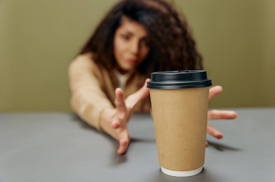 Woman reaching across a table for a takeaway coffee cup, cup in sharp focus and the person blurred in the background