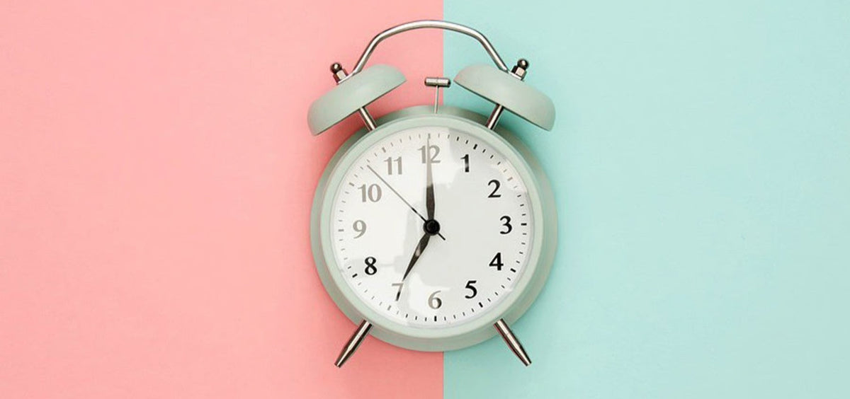 Mint-green twin-bell alarm clock centered on a split pink and light-blue background