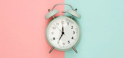 Mint-green twin-bell alarm clock centered on a split pink and light-blue background
