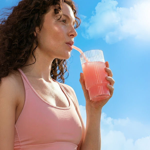 Woman sipping a pink drink from a ribbed glass with a straw against a bright blue sky