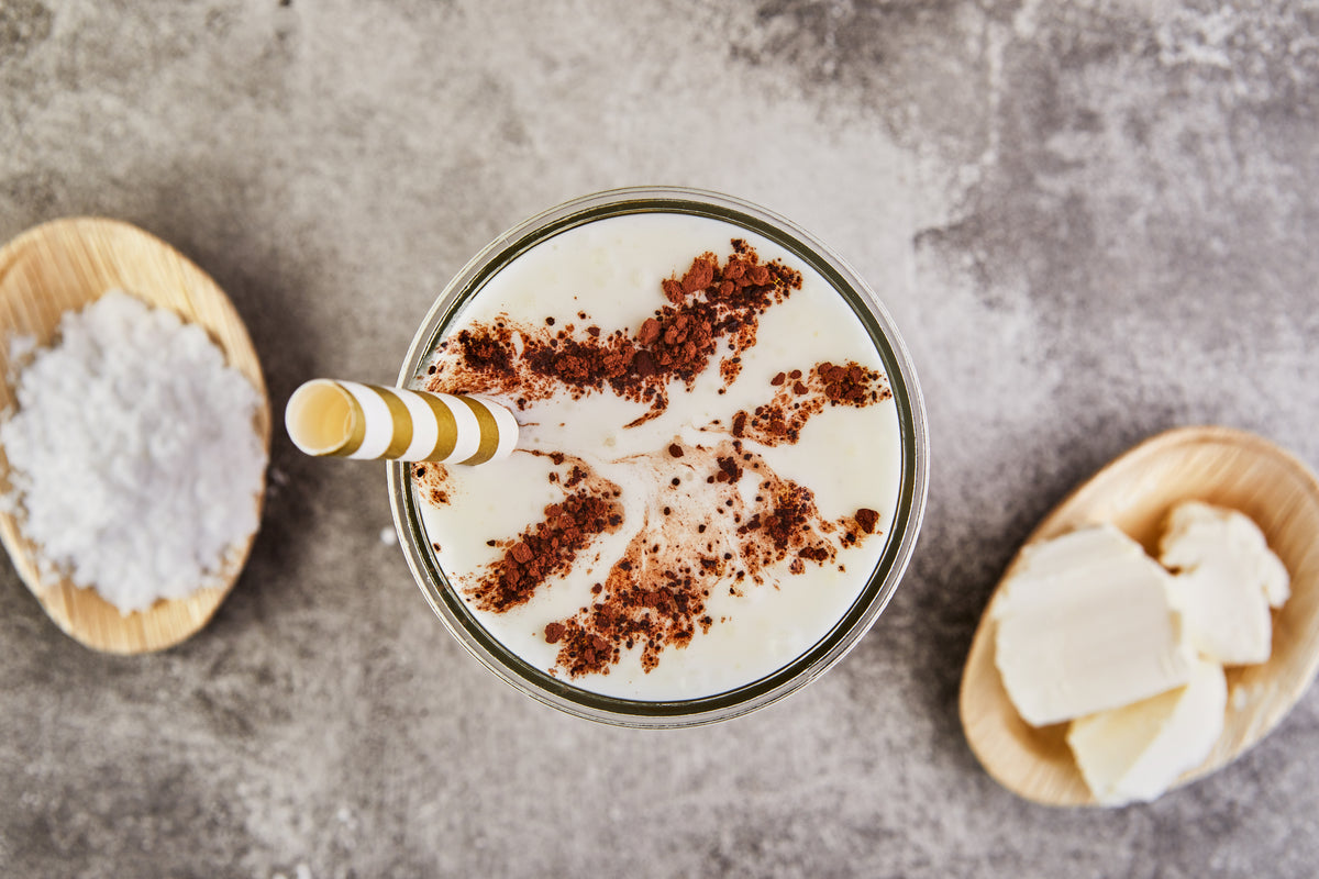 Top down view of iced almond chocolate drink with cocoa powder and striped straw on gray surface, coconut and almond pieces