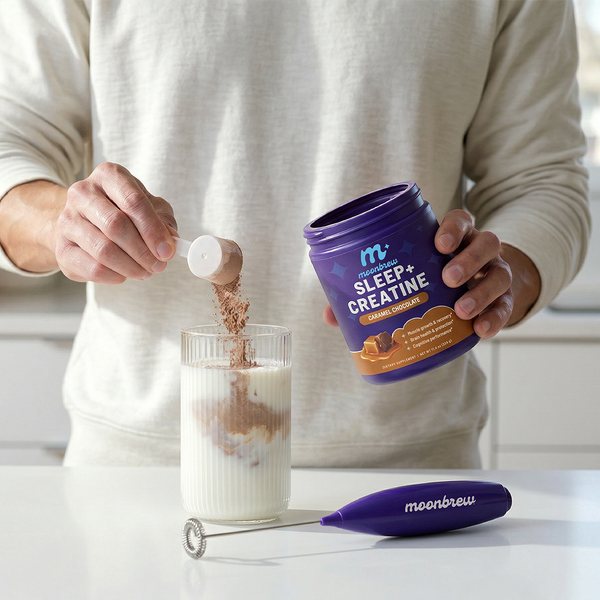 Hands pouring MoonBrew Sleep and Creatine powder from a purple container into a glass of milk on a bright kitchen counter