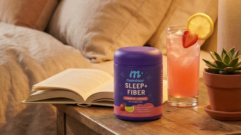 Front of MoonBrew Sleep+ Fiber tub highlighting the label with strawberry-lemon drink, book and succulent on a bedside table