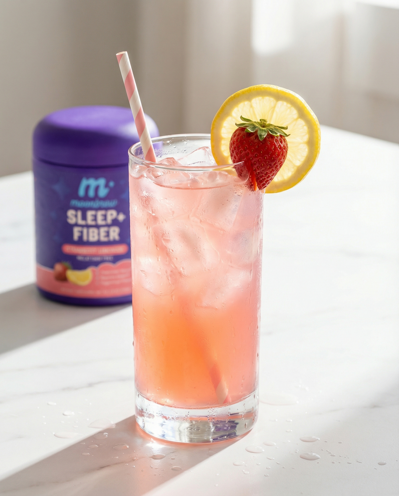 Tall glass of pink Strawberry Lemonade with ice, lemon slice and strawberry garnish, with MoonBrew Sleep+ Fiber tub in soft-focus background