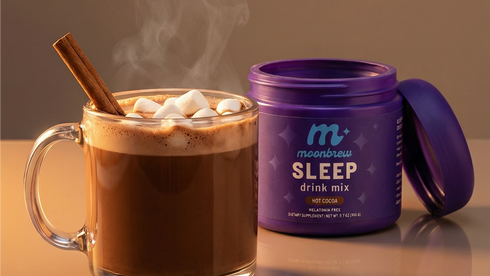 Three-quarter view of MoonBrew SLEEP drink mix tub next to a steaming mug of hot cocoa with marshmallows and cinnamon stick