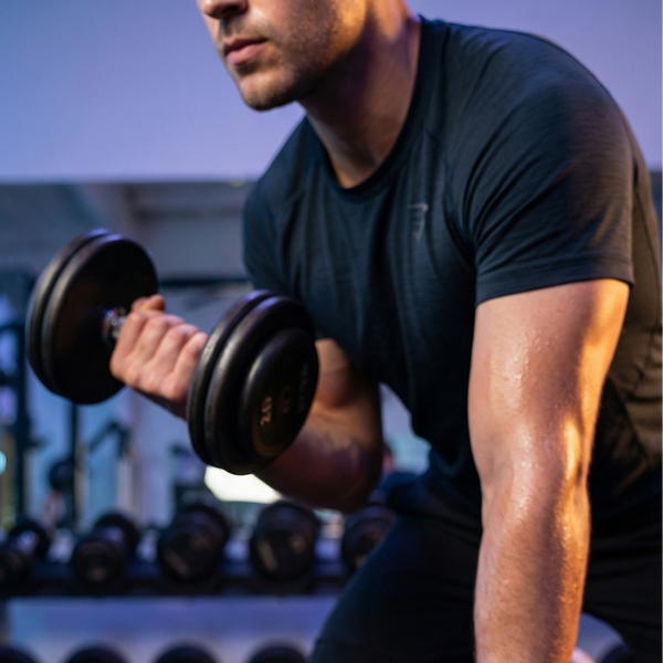 Man performing a one-arm dumbbell curl in a gym setting, sweaty forearm and rack of weights in the background