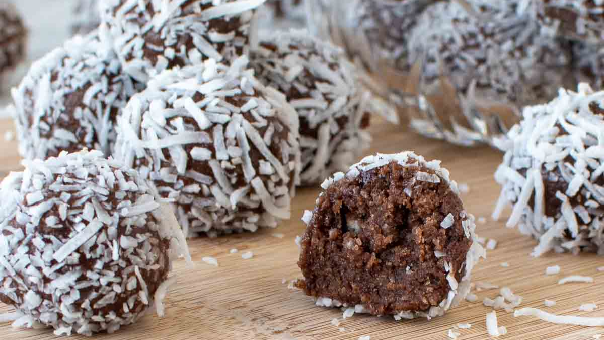 Close-up of Coconut Rum Balls showing shredded coconut coating and fudgy chocolate interior on a wooden cutting board