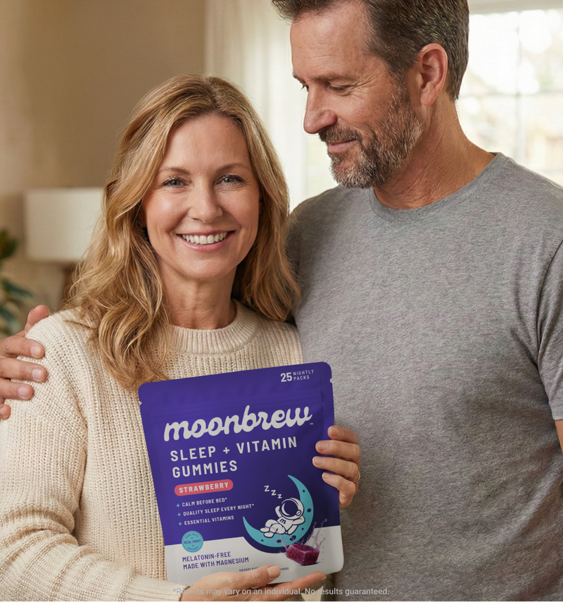 Middle-aged couple smiling and holding a MoonBrew Sleep and Vitamin Gummies strawberry pouch in a cozy home setting