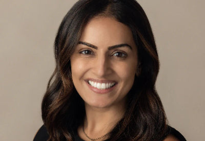 Dr. Roshini Malaney smiling in a head-and-shoulders portrait against a neutral beige background