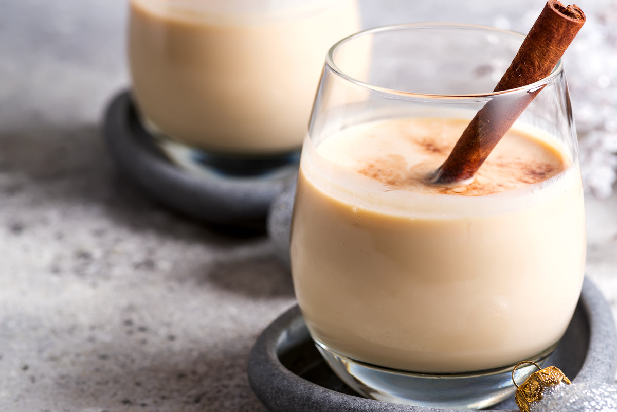 Glass of creamy Choco-Chata served over ice with a cinnamon stick on a gray stone coaster and a small holiday ornament